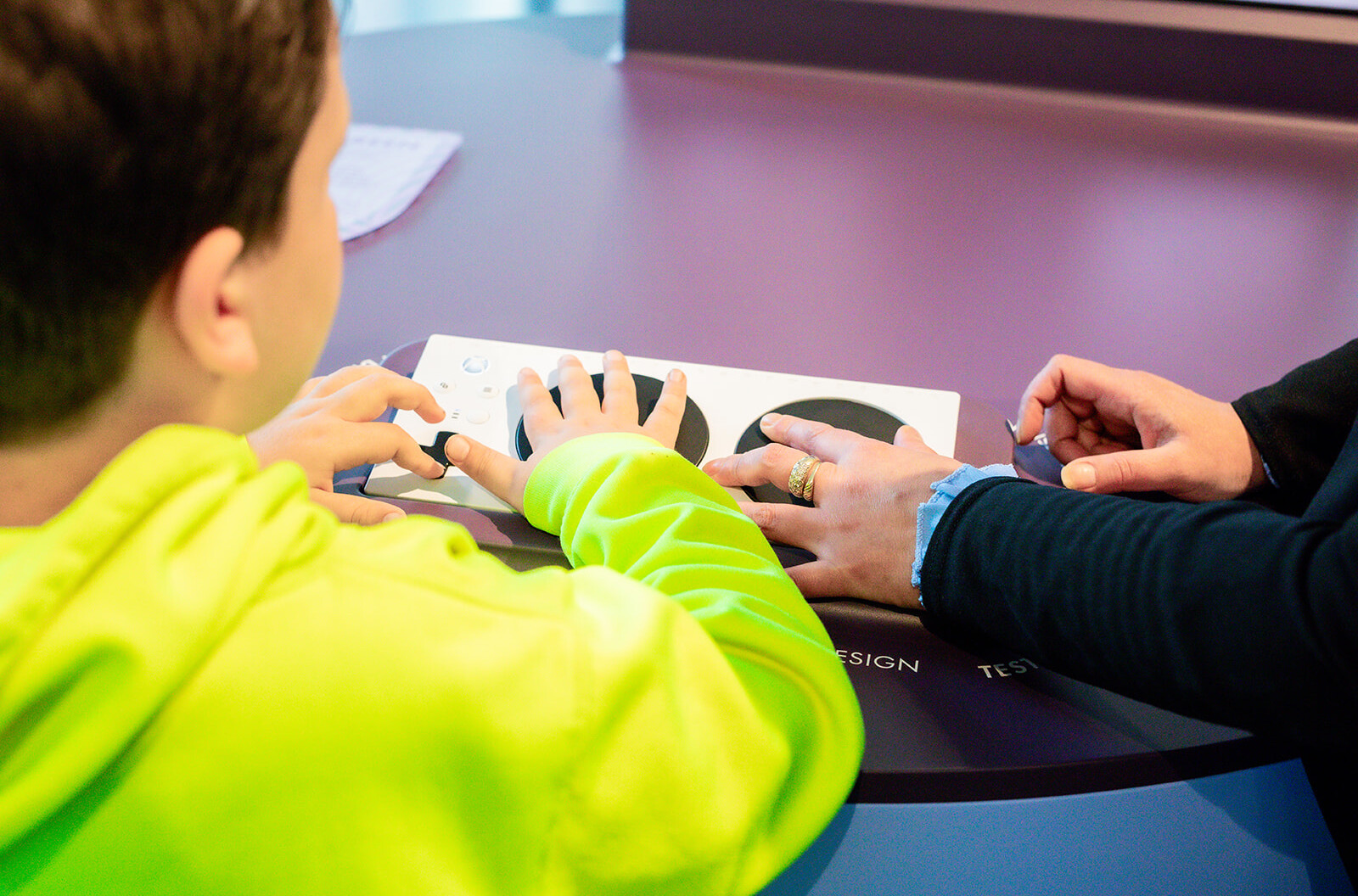 Een moeder en zoon spelen met een speciale Xbox controller in het OntwerpStation. Ze zijn van achter gefotografeerd.