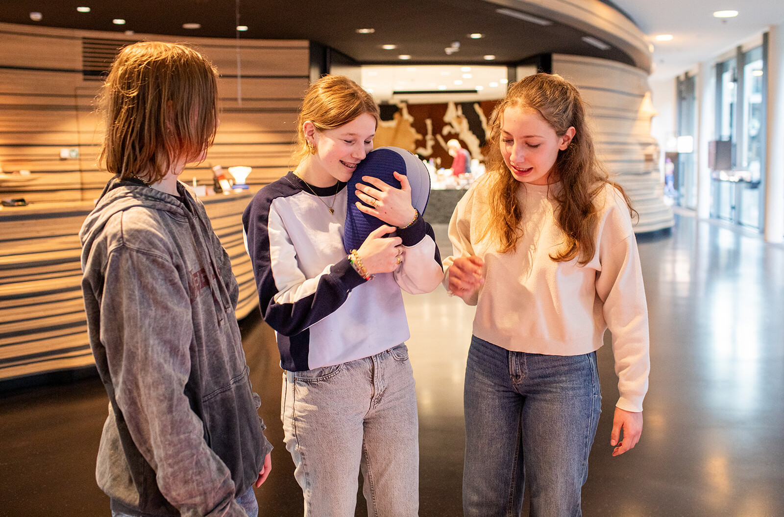 Drie meisjes houden een boonvormig kussen vast. Dit boonvormige kussen is een Somnox.